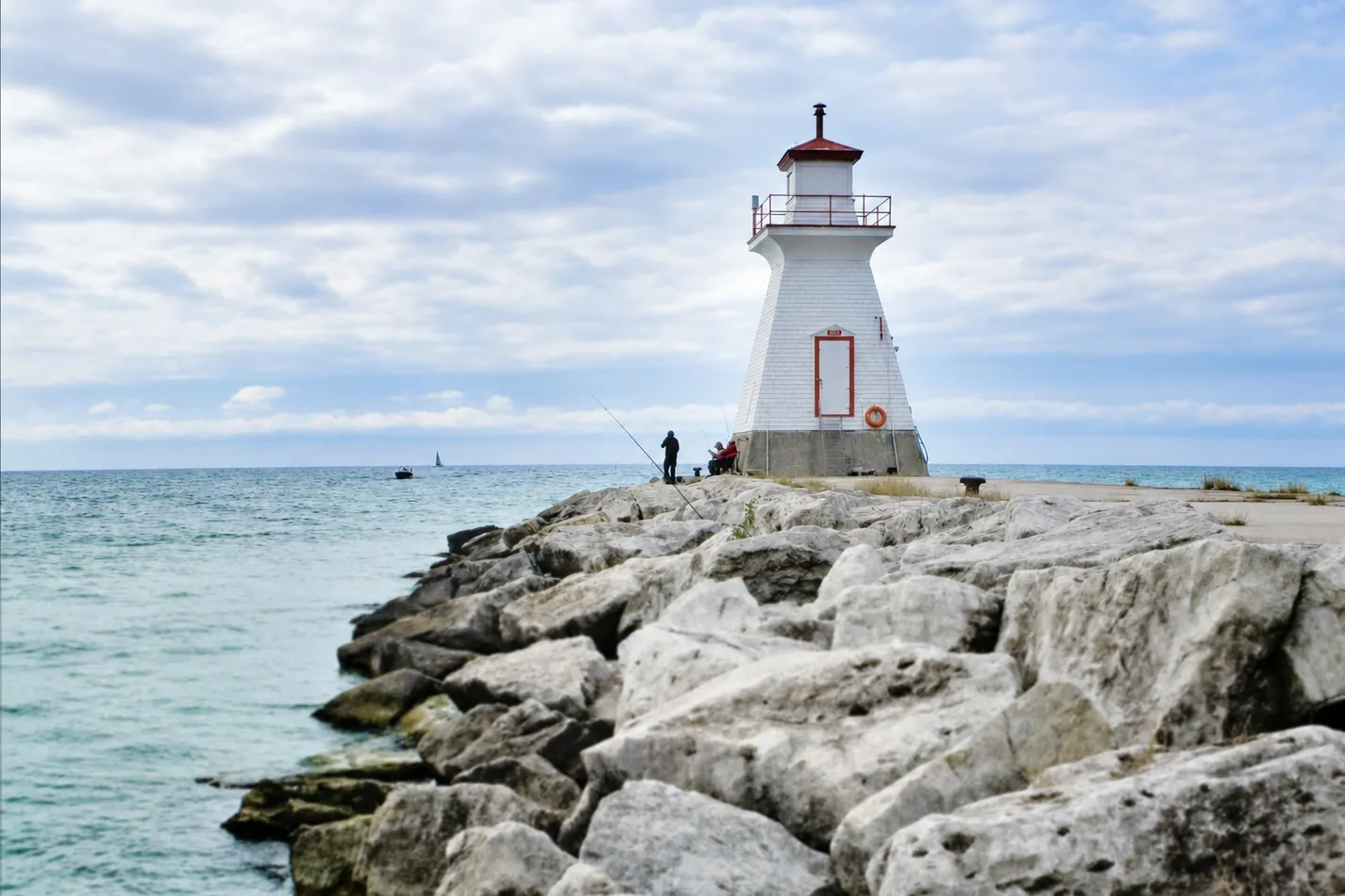 The white range light with its red lantern at the end of the breakwall, people fishing from the rocks below it