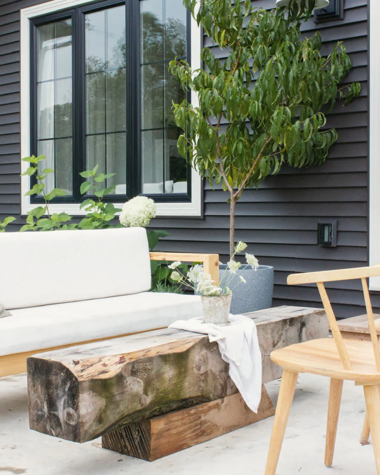 Chairs and a bench set out on a covered front porch beside dark siding