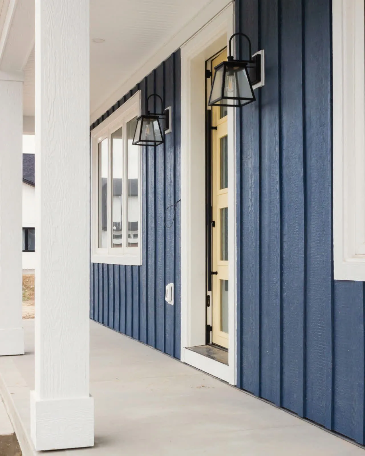 A porch column and front door against dark vertical siding: wood-look siding and a contrasting door