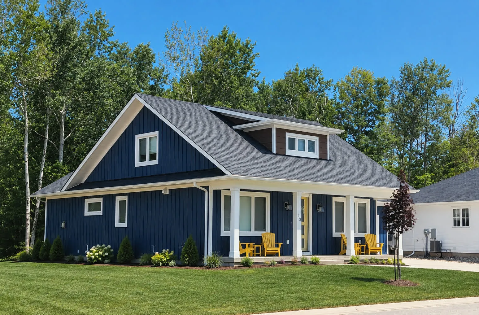 A navy storey-and-a-half home at Southampton Landing with yellow chairs set out on its covered front porch