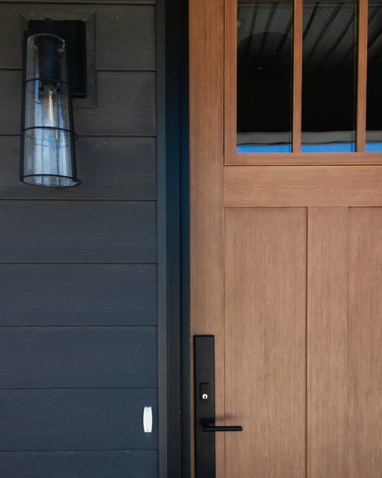 A wood front door beside dark board-and-batten siding