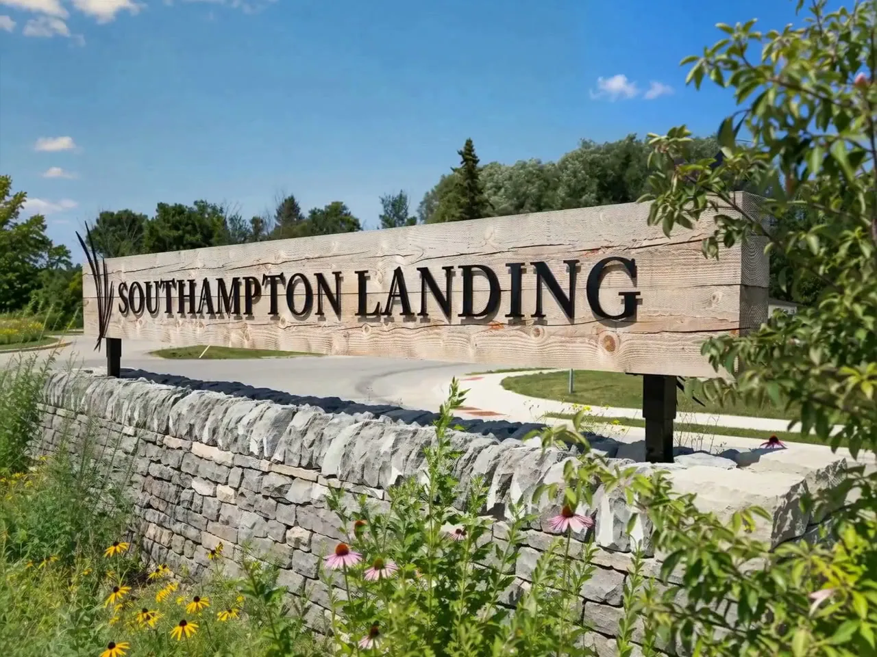 The Southampton Landing sign seen at an angle, its letters on a timber beam above a dry-stone wall, with summer planting grown in around it at the neighbourhood's entrance