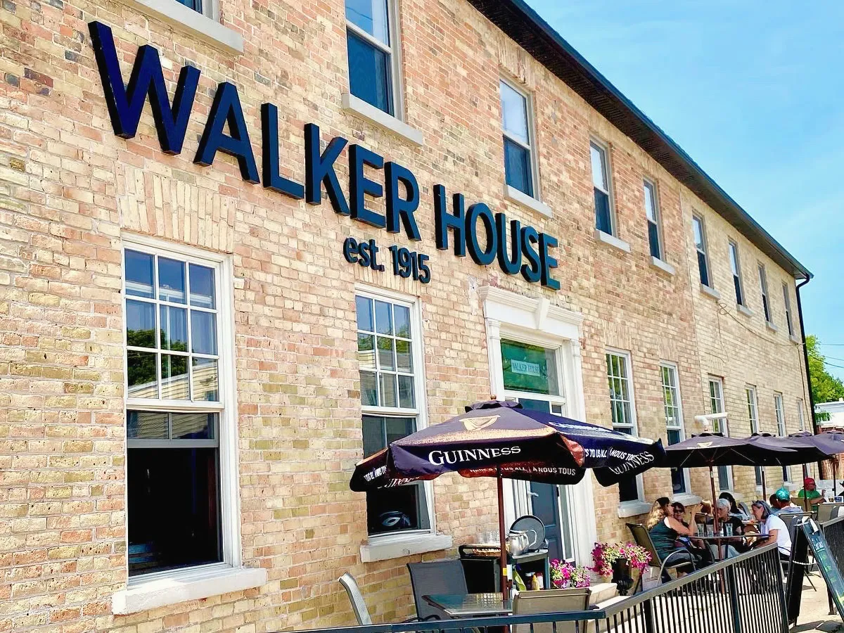 People on the patio of the Walker House on High Street, under its umbrellas, a yellow-brick building with est. 1915 on its sign